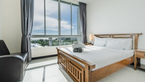 A hotel room with a large window, a bed with wooden headboard, a bedside table, and a chair.