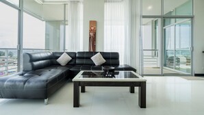 A modern living room with a black leather sectional sofa, a glass coffee table, and large floor-to-ceiling windows.