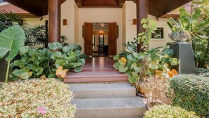 A covered entrance with steps leading to a doorway, surrounded by lush tropical plants.