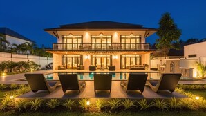 Une maison à deux étages avec une piscine, des chaises longues et un balcon bien éclairé.