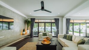 Un salon moderne doté d’une grande fenêtre, d’un ventilateur de plafond et d’un téléviseur à écran plat fixé au mur.