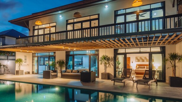 Une maison moderne à deux étages dotée d’une piscine, d’un espace salon extérieur et d’un balcon.