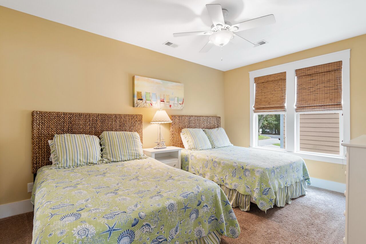 A bedroom with two beds, a ceiling fan, a nightstand, and a window with blinds.