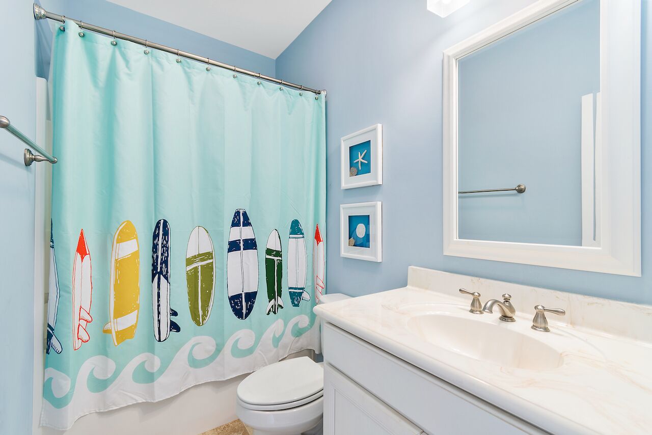 Ein Badezimmer mit hellblauer Wand, einem weißen Waschbecken und einer Duschvorhang mit Surfboard-Motiven.