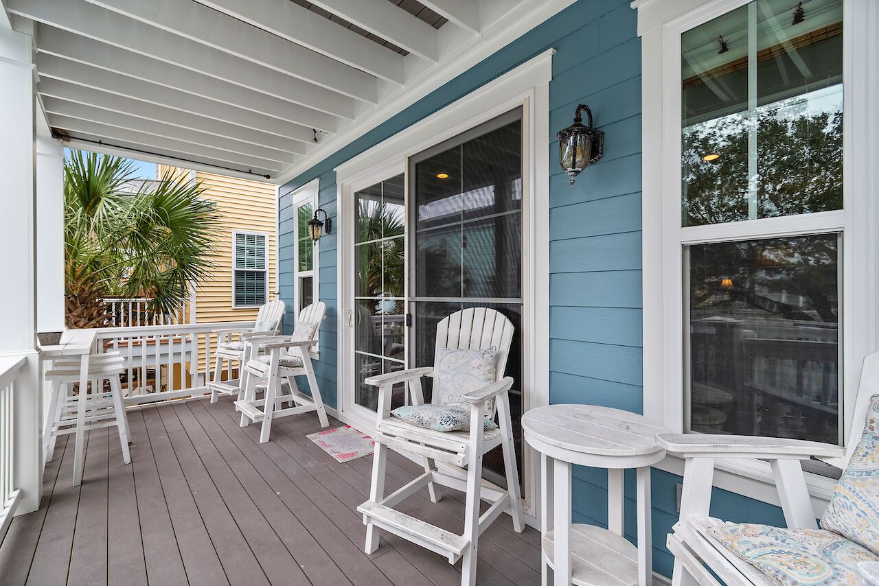 A covered porch with white Adirondack chairs and a small table, blue siding, and large windows.