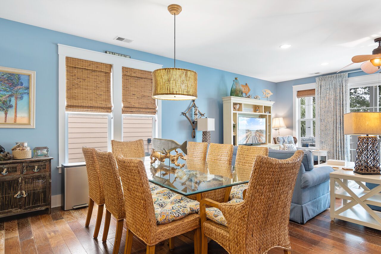 A dining area with a glass-top table surrounded by wicker chairs, a hanging light fixture, and a decorative mirror above the table.