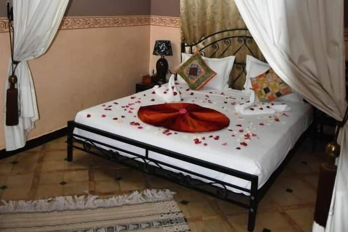 A four-poster bed with white and gold curtains, a patterned rug, and a bedside table with a lamp.