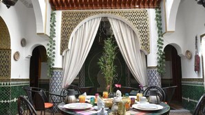 Un coin repas avec une table ronde dressée pour quatre personnes, entourée de chaises. La pièce est agrémentée d’arches décoratives et d’un sol carrelé à motifs.