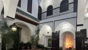 Une cour spacieuse agrémentée d’arcades traditionnelles, un espace de détente central avec des canapés et une table basse, et une vue sur l’intérieur à travers une arche ouverte.