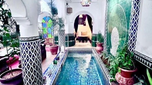 Un espace piscine agrémenté de motifs en mosaïque, de plantes en pot et d’un coin salon à l’arrière-plan.