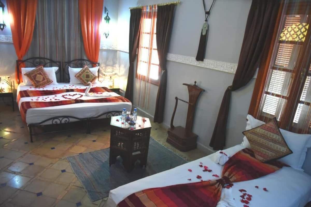 A hotel room with two beds, a small table with water bottles, and a decorative wall hanging.