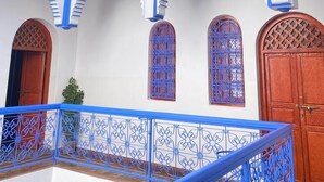 Une cour intérieure à plusieurs niveaux, avec des murs blancs et des touches de bleu, agrémentée de portes en arc de cercle et d’une balustrade bleue.