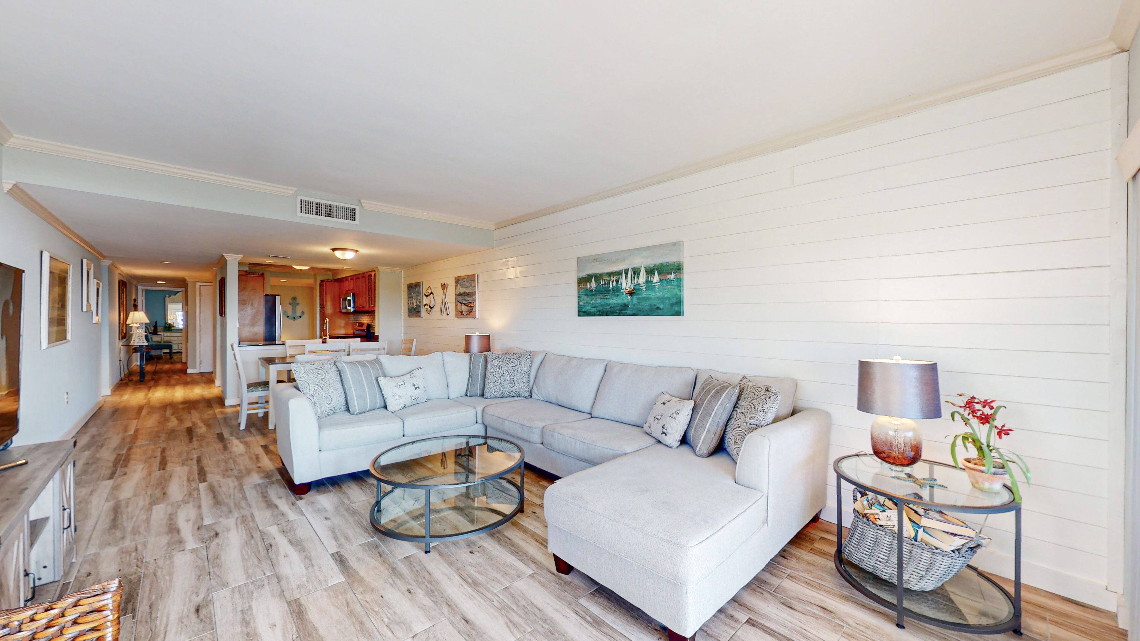A modern living room with a sectional sofa, a glass coffee table, and a dining area in the background.