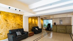 A modern lobby with a black leather sofa, a wooden accent wall, a reception desk, and a clear view into the kitchen area. - HANNA Balneário Hotel (Balneário Camboriú)