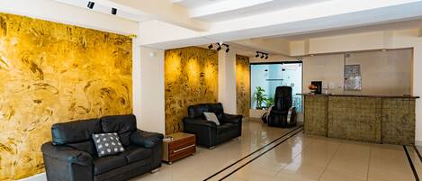 A modern lobby with a black leather sofa, a wooden accent wall, a reception desk, and a clear view into the kitchen area.