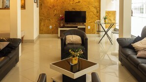 A modern living room with a black leather sofa, a glass coffee table, and a TV on a stand. - HANNA Balneário Hotel (Balneário Camboriú)