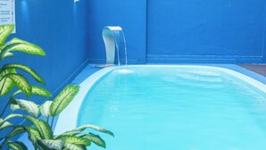 A swimming pool with a water feature, surrounded by blue walls and green plants. - HANNA Balneário Hotel (Balneário Camboriú)