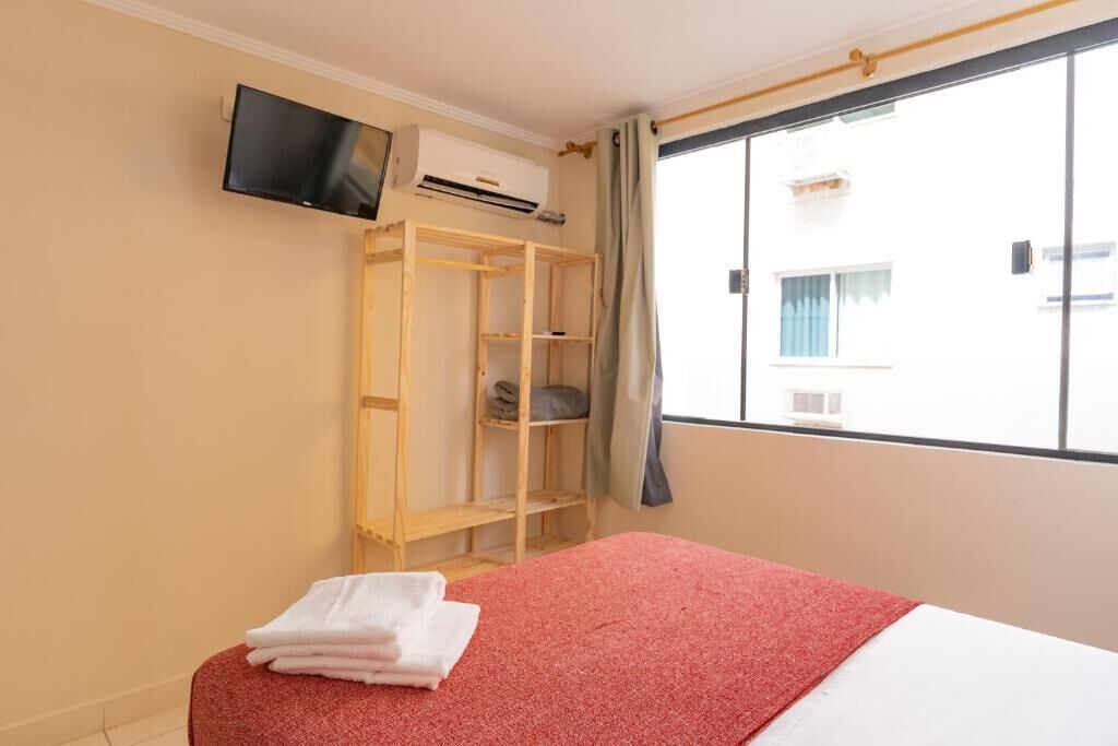 A hotel room with a bed, a TV mounted on the wall, a wardrobe, and a window with curtains.