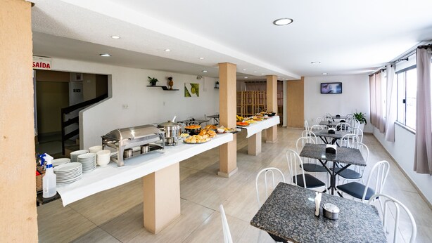 A buffet setup with multiple serving stations, white chairs, and a staircase leading to an upper level. - HANNA Balneário Hotel (Balneário Camboriú)