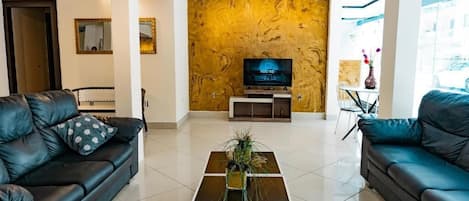 Un salón moderno con televisor de pantalla plana, dos sofás de cuero, una mesa de centro con un jarrón y un ventanal con vistas.
