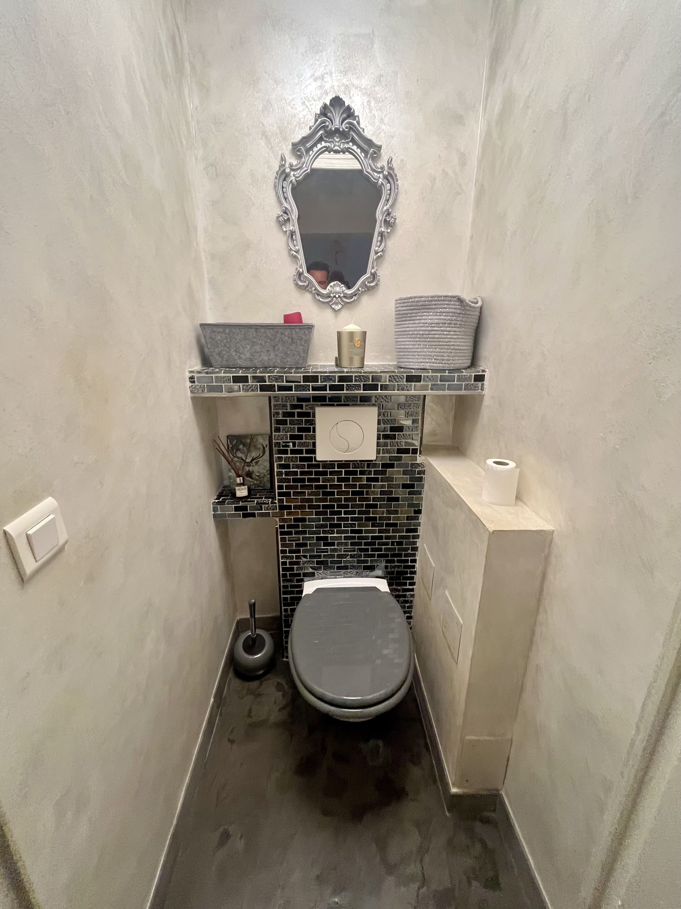 Ein kleines Badezimmer mit Toilette, Waschbecken mit Spiegel und Ablagefläche für Toilettenartikel.
