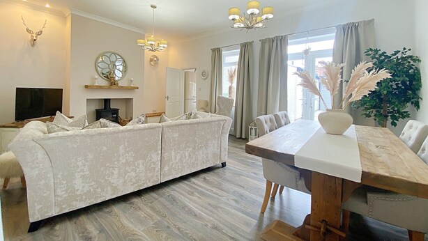 A spacious living room with a large sofa, a wooden dining table, and a chandelier. - Captivating 2-bed Cottage in Roker Sunderland (Sunderland)