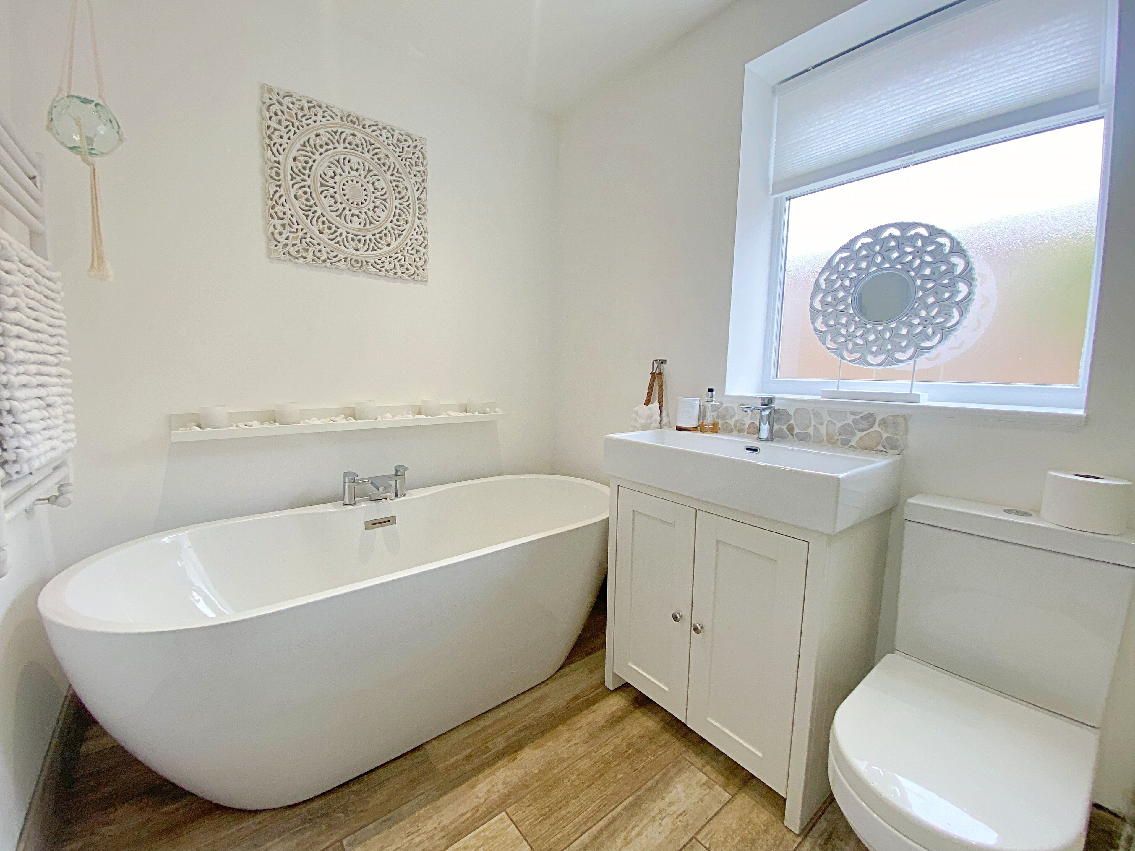 Een moderne badkamer met een vrijstaand bad, toilet en een wastafel met decoratieve wandkunst erboven.