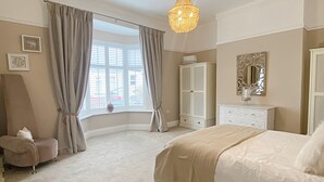 A bedroom with a large bed, a wardrobe, a vanity with a mirror, and a window with curtains. - Captivating 2-bed Cottage in Roker Sunderland (Sunderland)