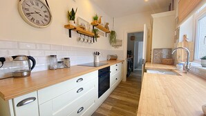 A modern kitchen with wooden countertops, white cabinets, and a hanging wall clock. - Captivating 2-bed Cottage in Roker Sunderland (Sunderland)