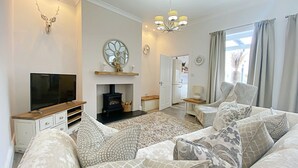 A living room with a fireplace, sofa, television, and decorative wall art. - Captivating 2-bed Cottage in Roker Sunderland (Sunderland)