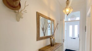 A hallway with a wooden console table, a mirror, a vase with branches, and a deer head decoration. - Captivating 2-bed Cottage in Roker Sunderland (Sunderland)