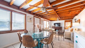 A spacious living area with a high ceiling, wooden beams, a round glass table with chairs, a television, and a sofa. - Oh So Sandy! - Southern Shores, Historic Flat Top, 100 Yds to Beach, Pets OK, Flex Stays (Southern Shores)