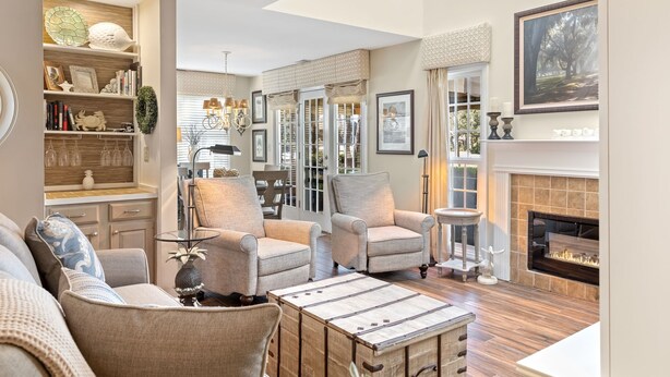 A spacious living room with a fireplace, comfortable seating, and a dining area visible through glass doors.