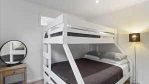 Un lit superposé avec une table de chevet en bois et un miroir, une lampe sur pied et une fenêtre avec des stores.