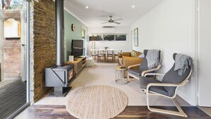 Un salon moderne avec un mur en pierre, un poêle à bois, un ventilateur de plafond et un tapis rond.