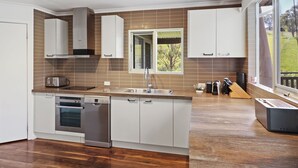 Une cuisine moderne dotée d’un îlot central, d’appareils électroménagers intégrés et d’une grande fenêtre offrant une vue sur l’extérieur.