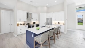 Une cuisine moderne avec des meubles blancs, un îlot central et des tabourets de bar.