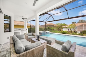 Ein überdachter Außenbereich mit Korbmöbeln, einem Pool und Blick auf die Nachbarhäuser.