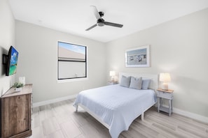 A bedroom with a bed, bedside tables, a ceiling fan, a TV, and artwork on the walls.