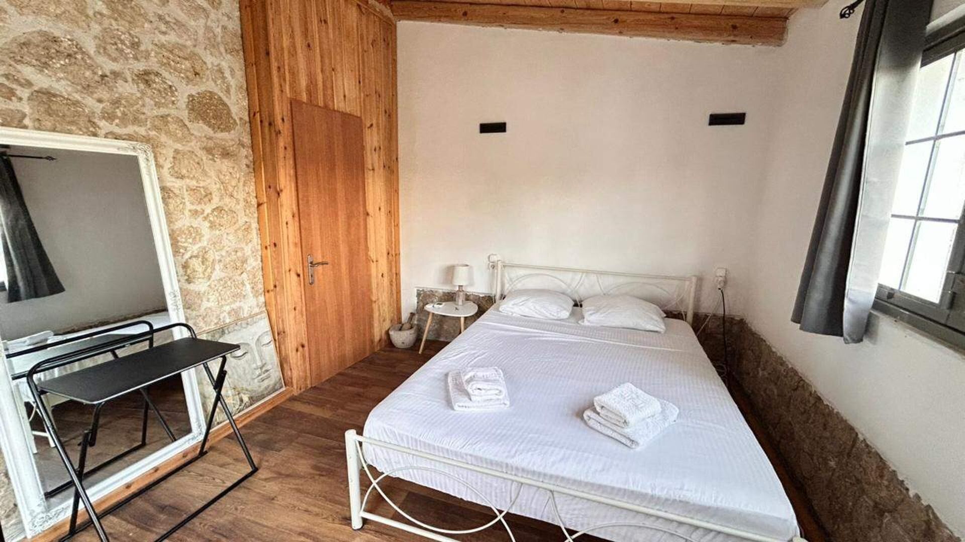 A bedroom with a bed, a small bedside table, a lamp, and a mirror.