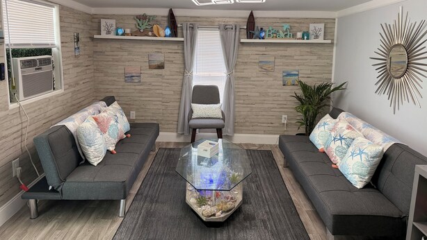Ein modernes Wohnzimmer mit zwei grauen Sofas, einem Glastisch und dekorativen Wandregalen.