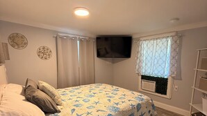 Ein Schlafzimmer mit einem Bett, Vorhängen, einem Flachbildfernseher, einem Fenster mit Vorhang und einem Regal.