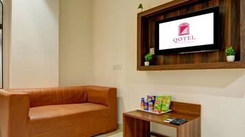 Ein Wohnzimmer mit einem braunen Ledersofa, einem Couchtisch mit Snacks, einem Fernseher an der Wand und einem kleinen Topfpflanzen.