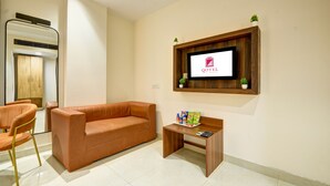 Un moderno vestíbulo de hotel con un sofá de madera, una mesita de madera con aperitivos, un televisor montado en un marco de madera y una planta pequeña en la pared.
