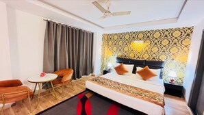 Una habitación de hotel con una cama, una pequeña mesa con sillas, un ventilador de techo y papel tapiz estampado.