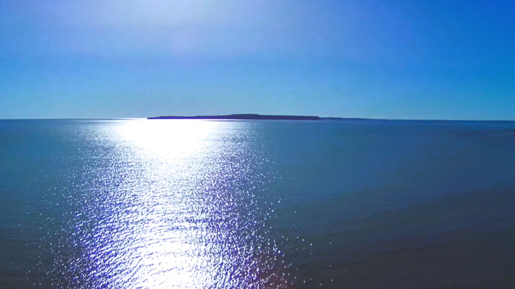 A calm sea with a clear sky and a distant landmass.