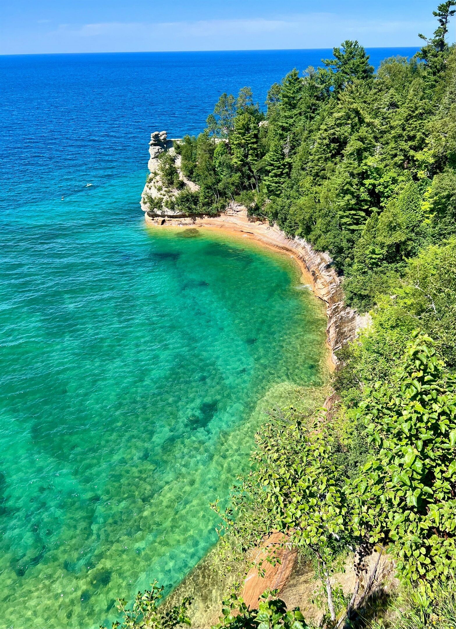 A coastal landscape with clear turquoise waters, a sandy beach, and dense green vegetation.