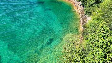 A coastal landscape with clear turquoise waters, a sandy beach, and dense green vegetation.