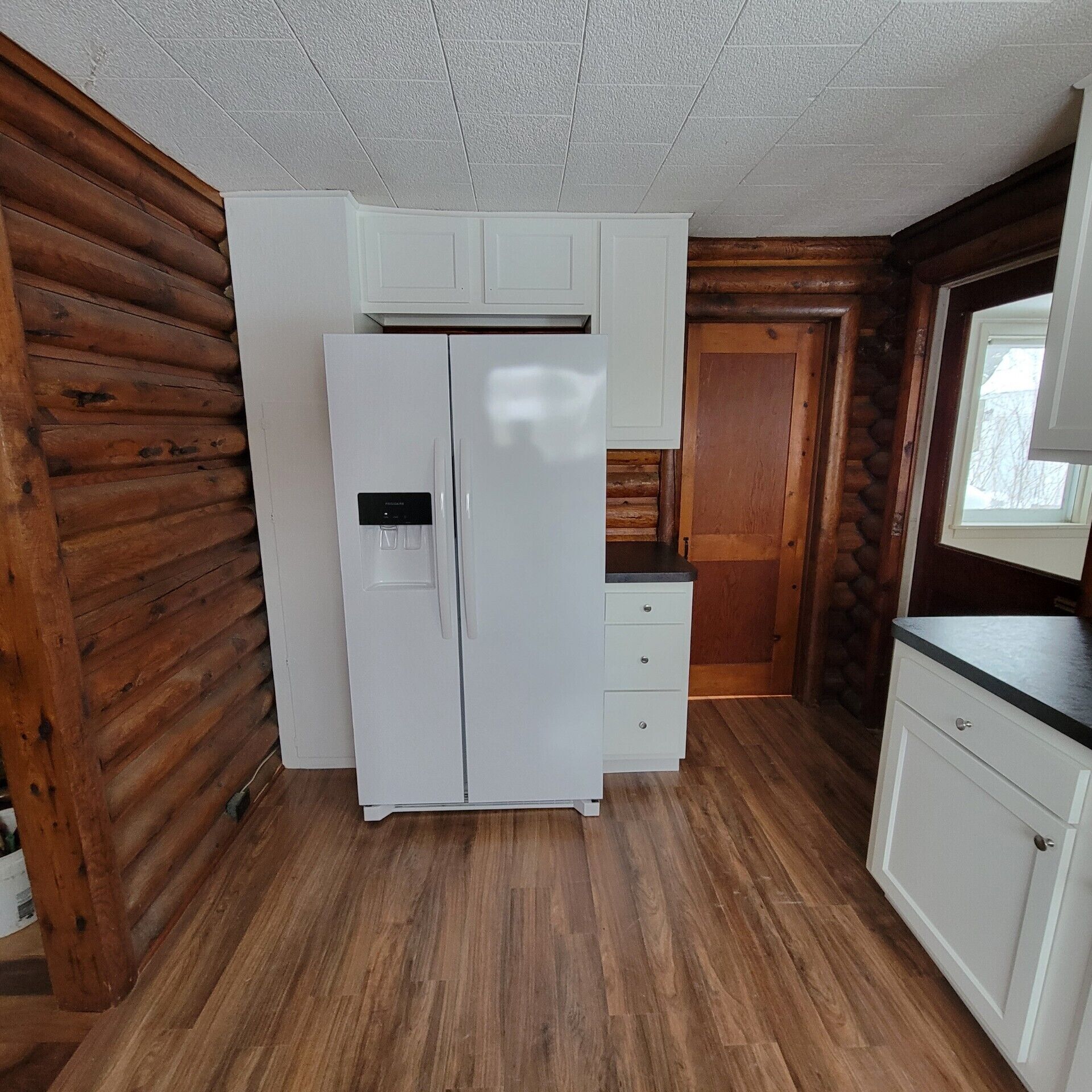 A compact kitchen with a white refrigerator, wooden cabinets, and a window.