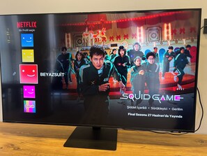 A television displaying the Netflix interface with the title "Squid Game" and a scene from the show. - Beyaz Suite (Midyat)